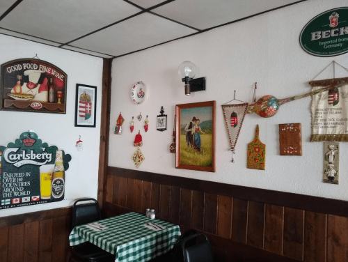 A cozy restaurant wall decorated with vintage signs, artwork, and cultural memorabilia, featuring a checkered tablecloth.