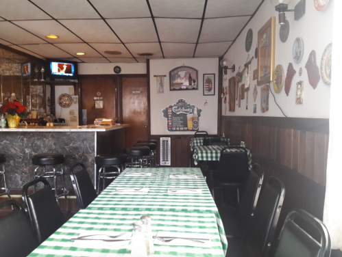 Interior of a cozy restaurant with checkered green and white tablecloths, a bar area, and vintage decor on the walls.