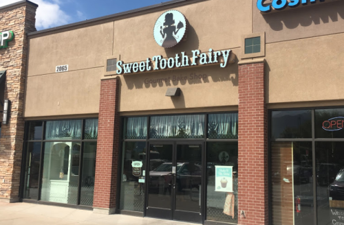 Exterior of Sweet Tooth Fairy, a gourmet bake shop, featuring a sign and large windows with curtains.