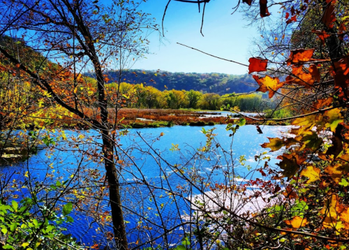 A serene lake surrounded by colorful autumn foliage and trees under a clear blue sky.