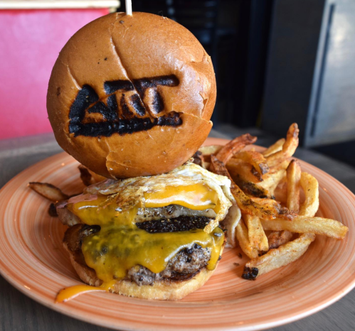 A juicy cheeseburger with a fried egg on top, served with crispy fries on an orange plate.