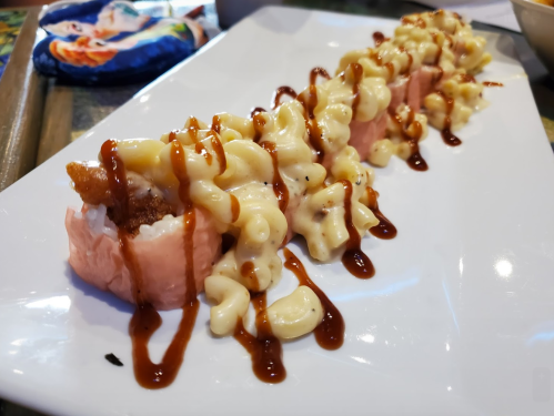 A plate of sushi rolls topped with creamy macaroni and cheese and drizzled with sauce.