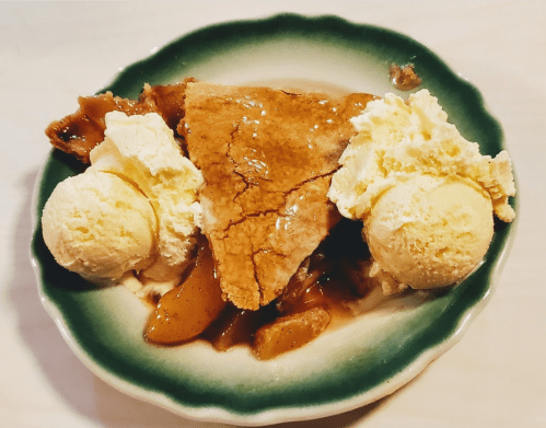A slice of apple pie topped with two scoops of vanilla ice cream on a green-rimmed plate.