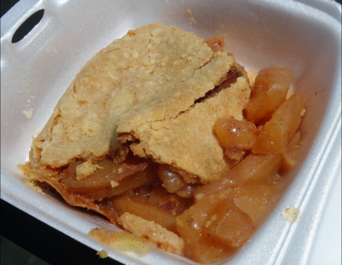 A serving of apple pie in a takeout container, with a flaky crust and visible apple filling.