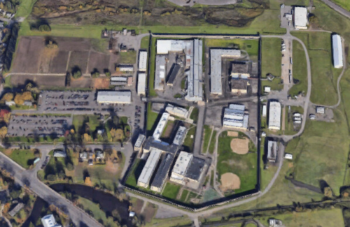 Aerial view of a large facility with multiple buildings, parking areas, and a baseball field surrounded by greenery.