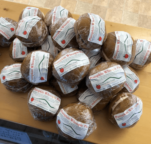 A pile of wrapped pumpkin whoopie pies with labels on a wooden table.