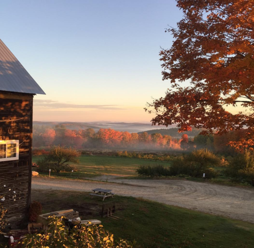 A scenic view of a farm at sunrise, with vibrant autumn foliage and mist over the fields in the background.