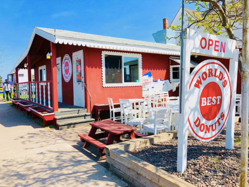 A red building with a sign reading "World's Best Donuts," featuring outdoor seating and a clear blue sky.