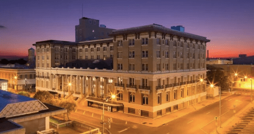 Historic building at sunset, illuminated by streetlights, with a vibrant purple sky in the background.