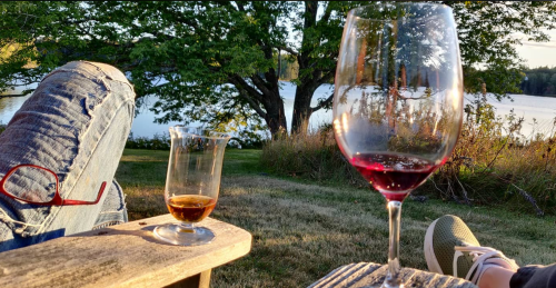 A close-up of two glasses on a wooden table, with a scenic view of a lake and trees in the background.