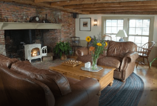 Cozy living room with leather sofas, a wooden coffee table, a fireplace, and large windows letting in natural light.