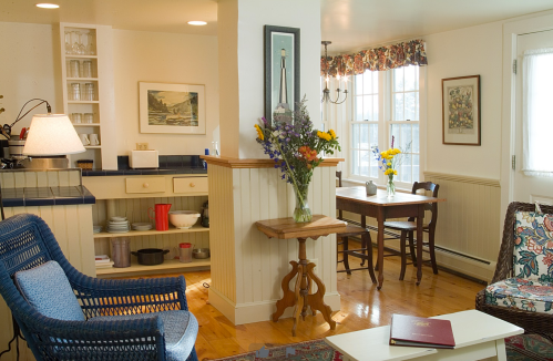 Cozy interior featuring a kitchen area, dining table with flowers, and a sitting area with colorful decor.