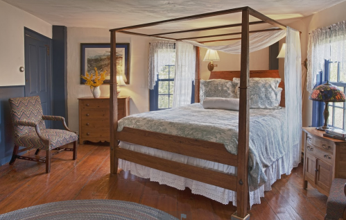 Cozy bedroom featuring a four-poster bed, patterned bedding, wooden furniture, and natural light from windows.