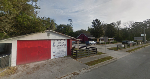 A diner and deli with a red exterior, surrounded by trees and parked cars on a quiet street.