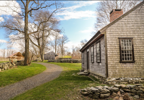 A scenic view of a pathway leading to rustic wooden buildings surrounded by trees and a clear blue sky.