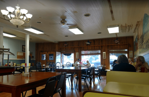 A cozy diner interior with wooden walls, tables, and patrons enjoying meals by the window.