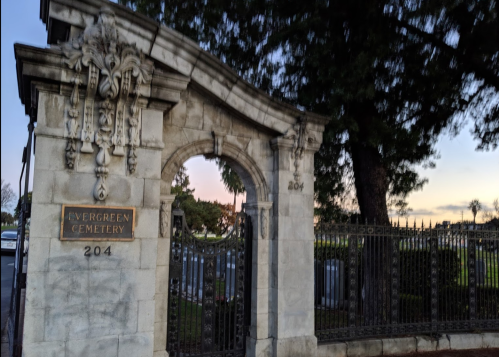 Stone archway of Evergreen Cemetery with a plaque reading "204" at sunset, surrounded by trees and gravestones.