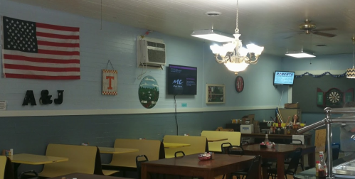 Interior of a casual restaurant with yellow tables, an American flag, and a dartboard on the wall.