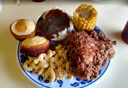 A plate of fried chicken, macaroni and cheese, corn on the cob, mashed potatoes with gravy, and cornbread muffins.