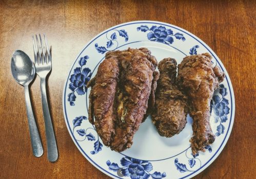 A plate with three pieces of crispy fried chicken, accompanied by a fork and knife on a wooden table.