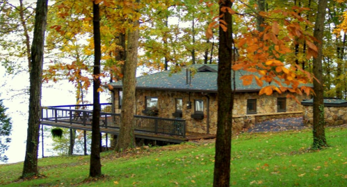 A stone cabin surrounded by colorful autumn trees, overlooking a serene lake.
