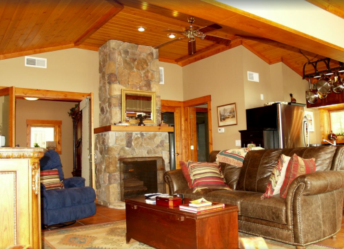 Cozy living room with a stone fireplace, brown sofa, blue chair, and wooden ceiling, creating a warm atmosphere.