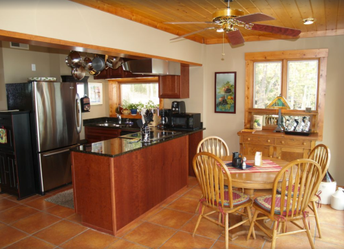 Cozy kitchen with wooden accents, black appliances, and a dining table set for four. Natural light from a window.