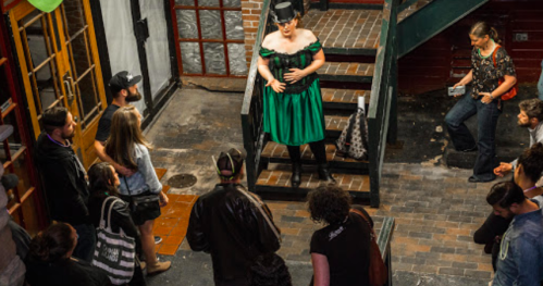 A performer in a green dress entertains a crowd on stairs in a lively indoor venue.