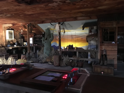 Interior of a rustic western-themed room with a mural of a sunset, cacti, and various vintage decor items.