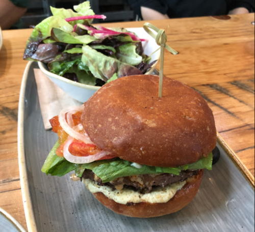 A gourmet burger with lettuce, tomato, and onion, served on a plate with a side salad.