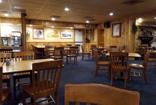 Cozy restaurant interior with wooden tables and chairs, rustic decor, and a fireplace in a warm, inviting atmosphere.