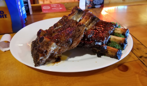 A plate of grilled ribs with a charred glaze, served on a wooden table.