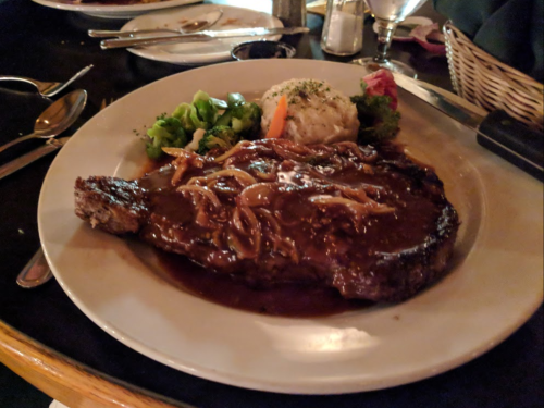 A plate featuring a juicy steak with onion gravy, served with broccoli and mashed potatoes, garnished with a carrot.