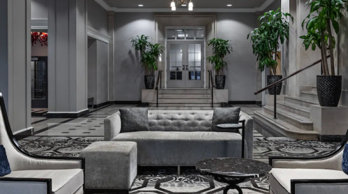 Modern hotel lobby featuring a gray sofa, marble coffee table, and potted plants, with elegant decor and lighting.