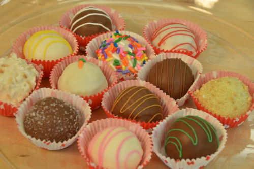 A variety of colorful chocolate truffles arranged in pink paper cups, featuring different toppings and designs.