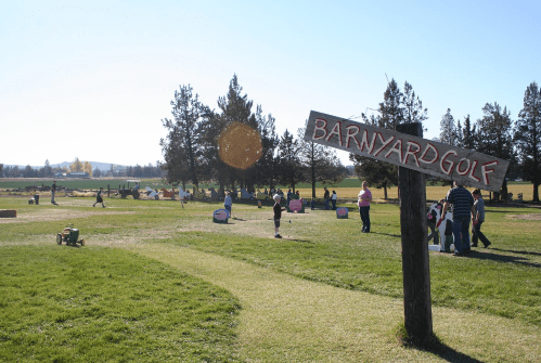 A sunny day at a barnyard golf course with people playing and a sign reading "Barnyard Golf" in the foreground.