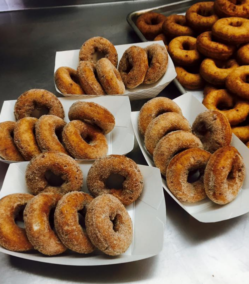 Four trays of freshly made, cinnamon-sugar coated donuts arranged neatly on a countertop.