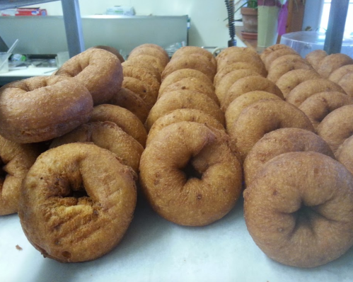 A close-up of freshly made, golden-brown donuts arranged in a row on a countertop.