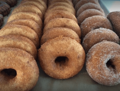 A variety of freshly made donuts arranged in rows, some plain and others coated in sugar.