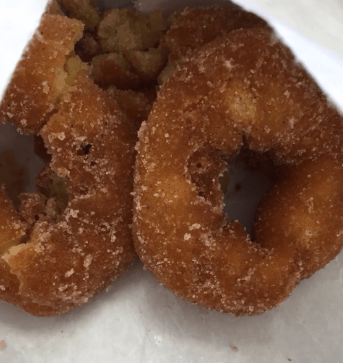 Two sugar-coated donuts with a golden-brown color, partially visible in a white bag.