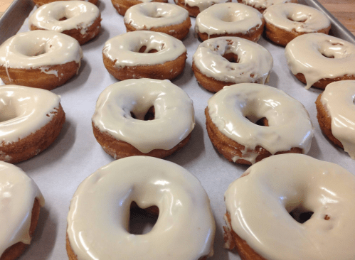 A tray of freshly glazed donuts with a light brown icing, arranged in neat rows.