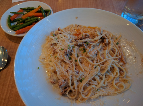A plate of creamy pasta topped with cheese, served with a side of green beans and carrots.