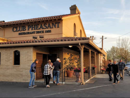 A group of people entering Club Pheasant restaurant, featuring a warm exterior and flower planters.