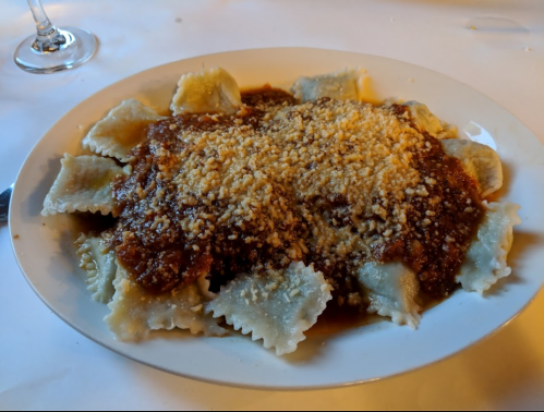 A plate of ravioli topped with a rich meat sauce and sprinkled with grated cheese, served on a white table.