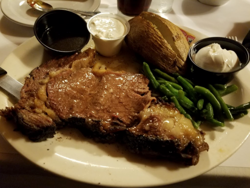 A plate featuring a juicy steak, baked potato with sour cream, and green beans, served with dipping sauces.