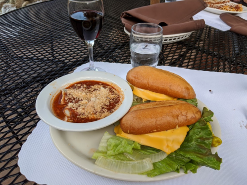 A plate with two cheese sandwiches on lettuce, a bowl of sauce with toppings, a glass of water, and a glass of red wine.