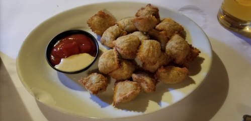 A plate of golden-brown fried ravioli served with ketchup and a creamy dipping sauce.