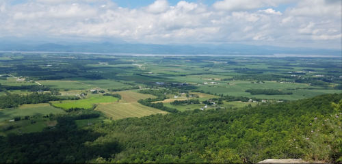 A panoramic view of lush green fields and distant mountains under a partly cloudy sky.