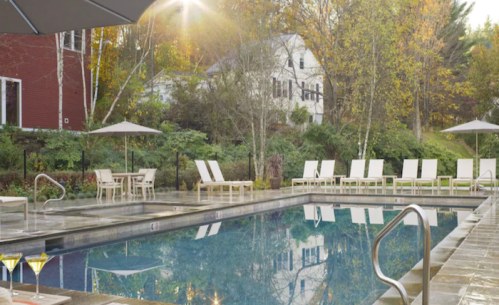 A serene outdoor pool area surrounded by trees, with lounge chairs and umbrellas, reflecting autumn colors.