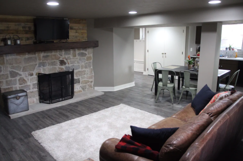 Cozy living space with a stone fireplace, leather sofa, and dining area featuring a table and chairs.